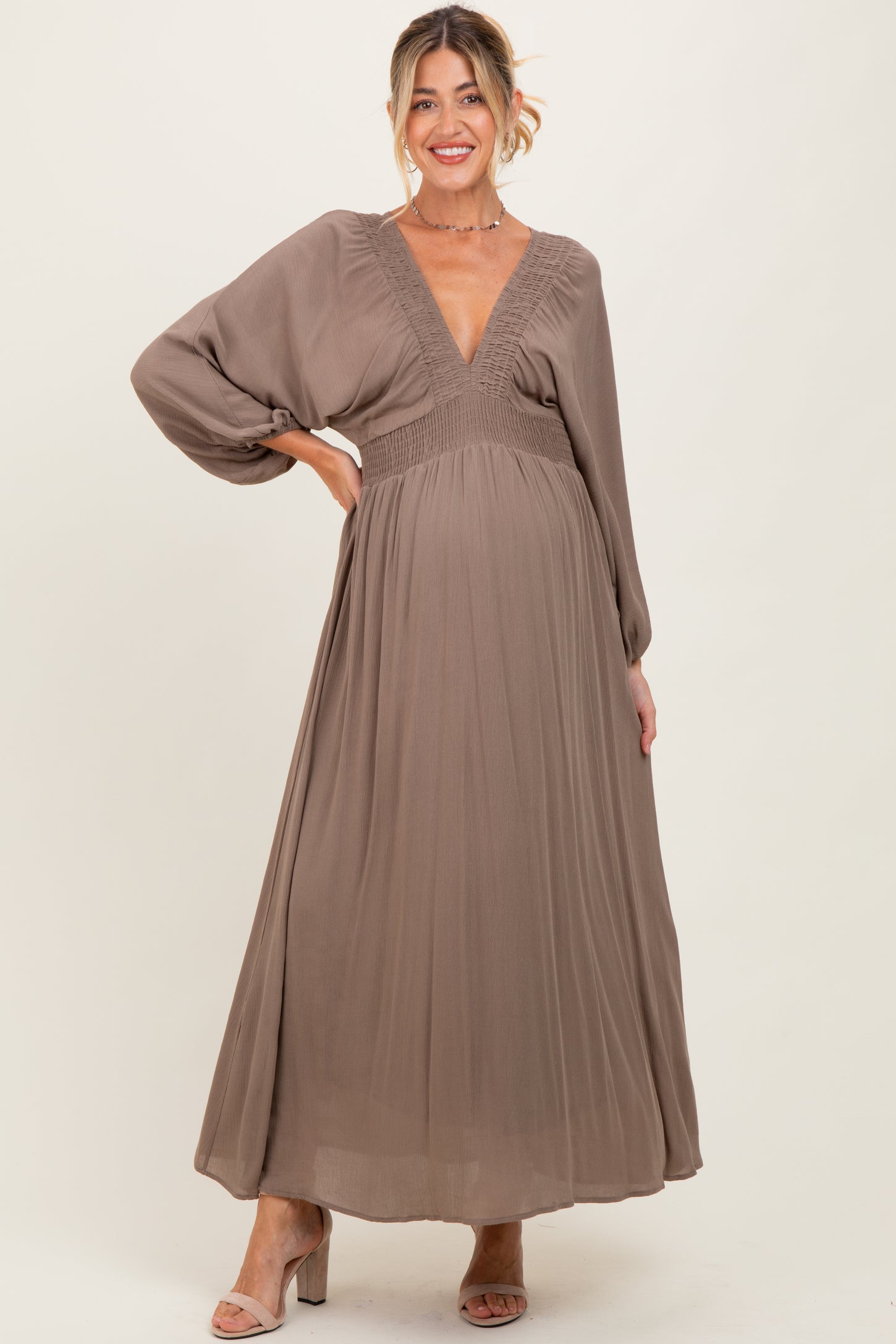 woman wearing a taupe long sleeve maternity maxi dress with a deep v-neck and smocked waist, showing her baby bump