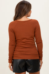 woman wearing a rust colored long sleeve maternity top with a fitted style and gathered detail at the sides