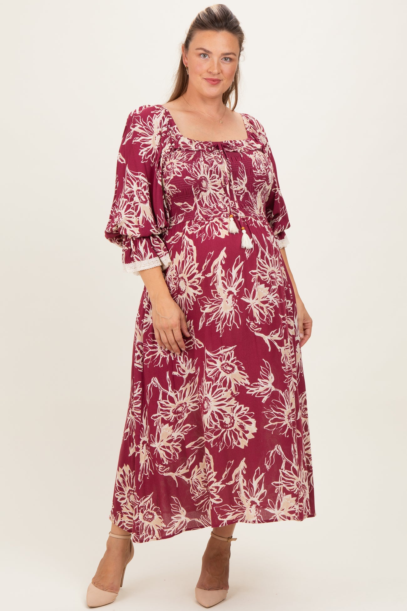 woman wearing a burgundy floral maternity dress with a square neckline and bell sleeves, showcasing a baby bump