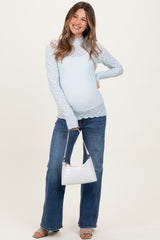 woman wearing a light blue maternity long sleeve top with textured details, paired with flared jeans and holding a white handbag
