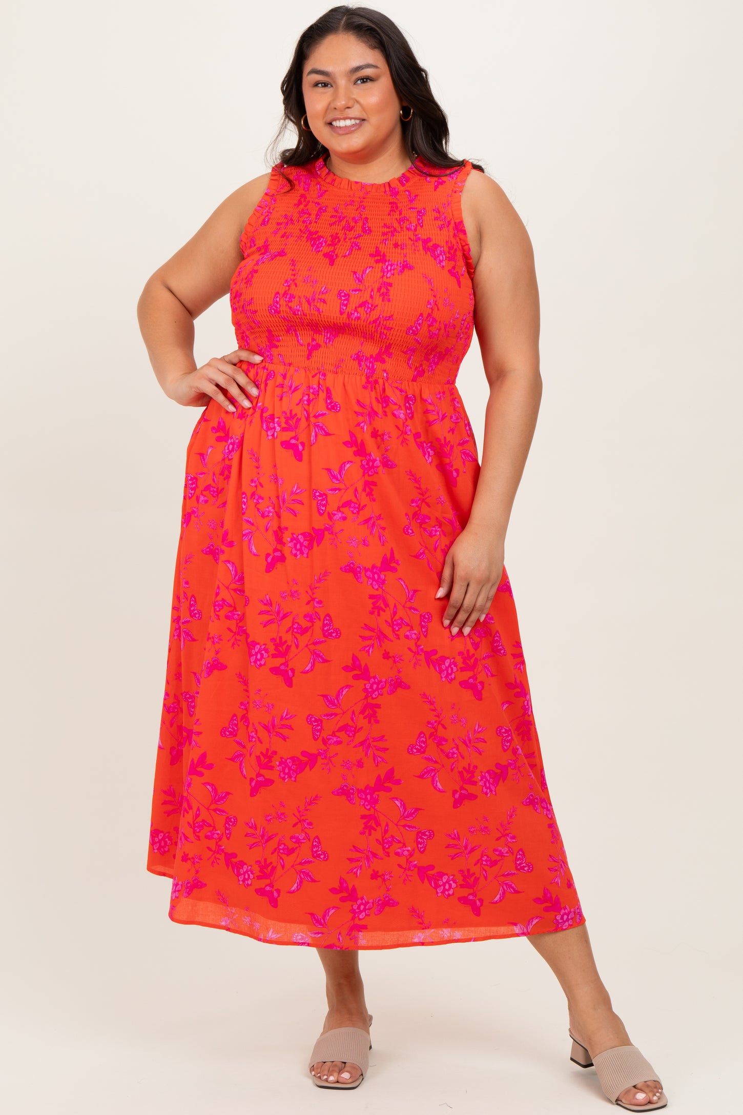 woman wearing a bright orange floral print plus size maxi dress with smocking and ruffled shoulders