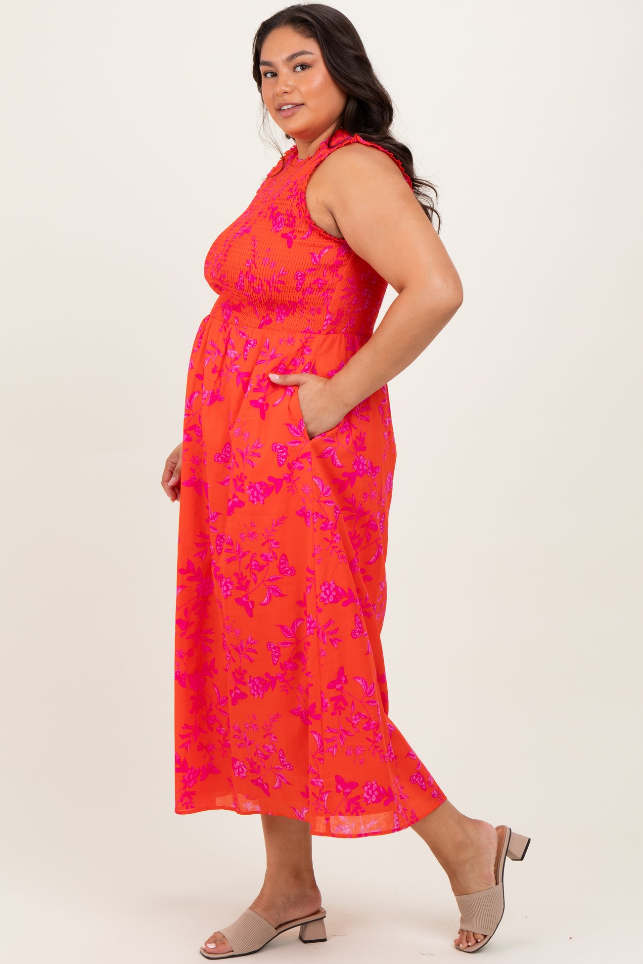 woman wearing a bright pink sleeveless plus size maxi dress with floral print and side pockets