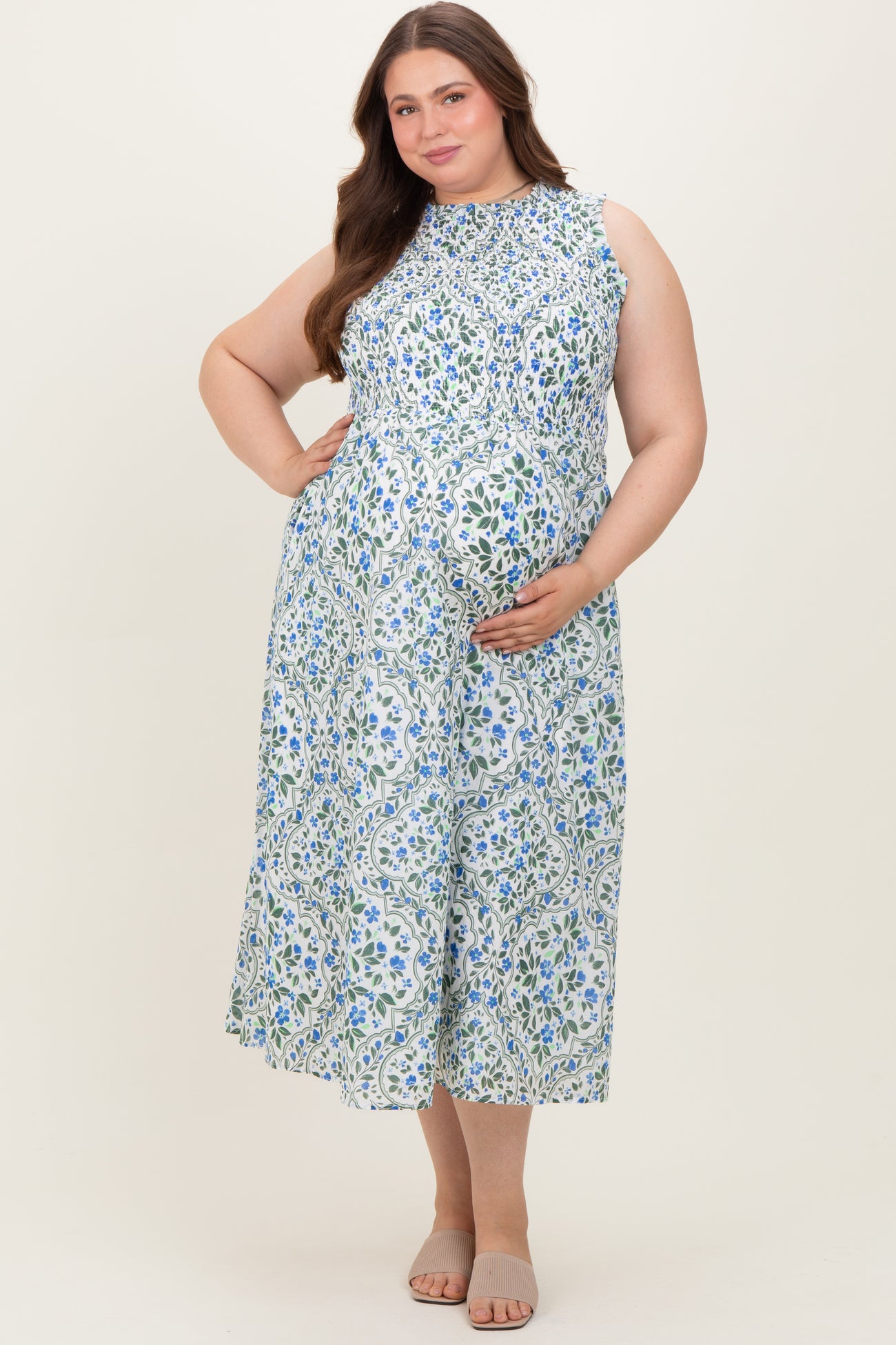 woman wearing a light blue floral sleeveless maternity dress and holding her baby bump