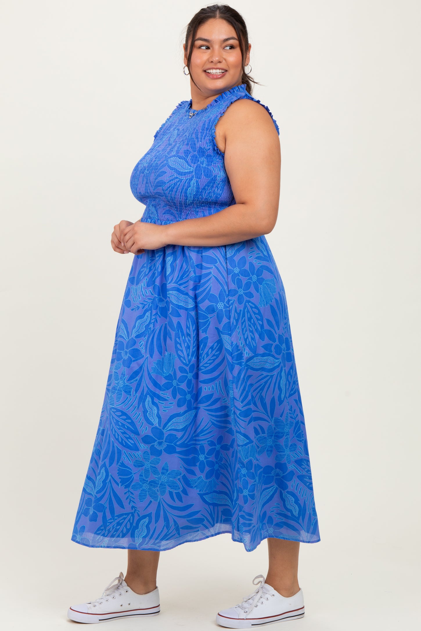 woman wearing a sleeveless blue floral plus size maxi dress with a smocked bodice and white sneakers