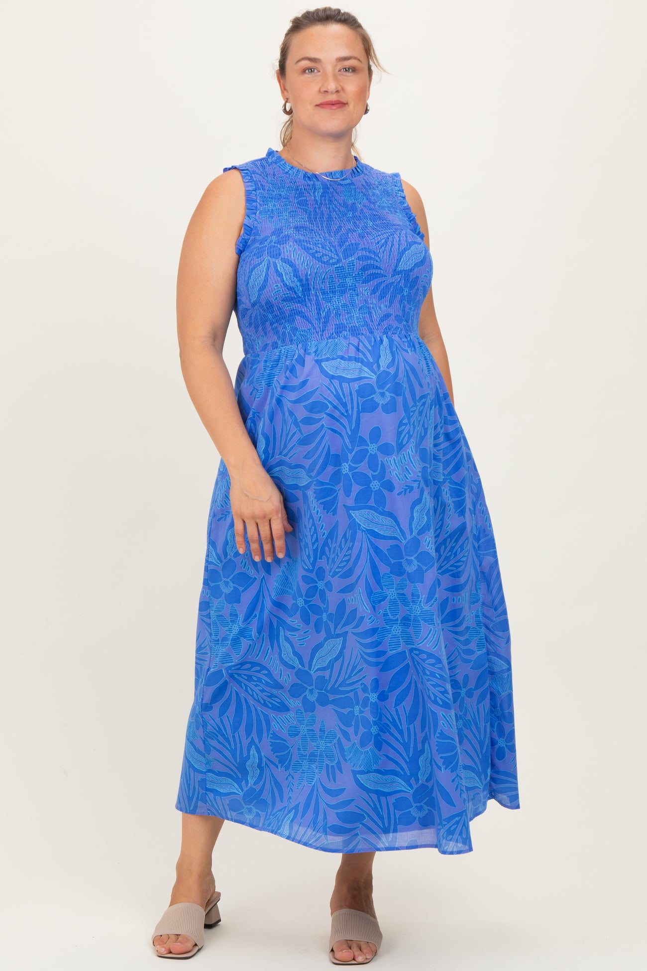 woman wearing a bright blue floral maternity dress with a smocked bodice and a flowing skirt, showcasing her baby bump