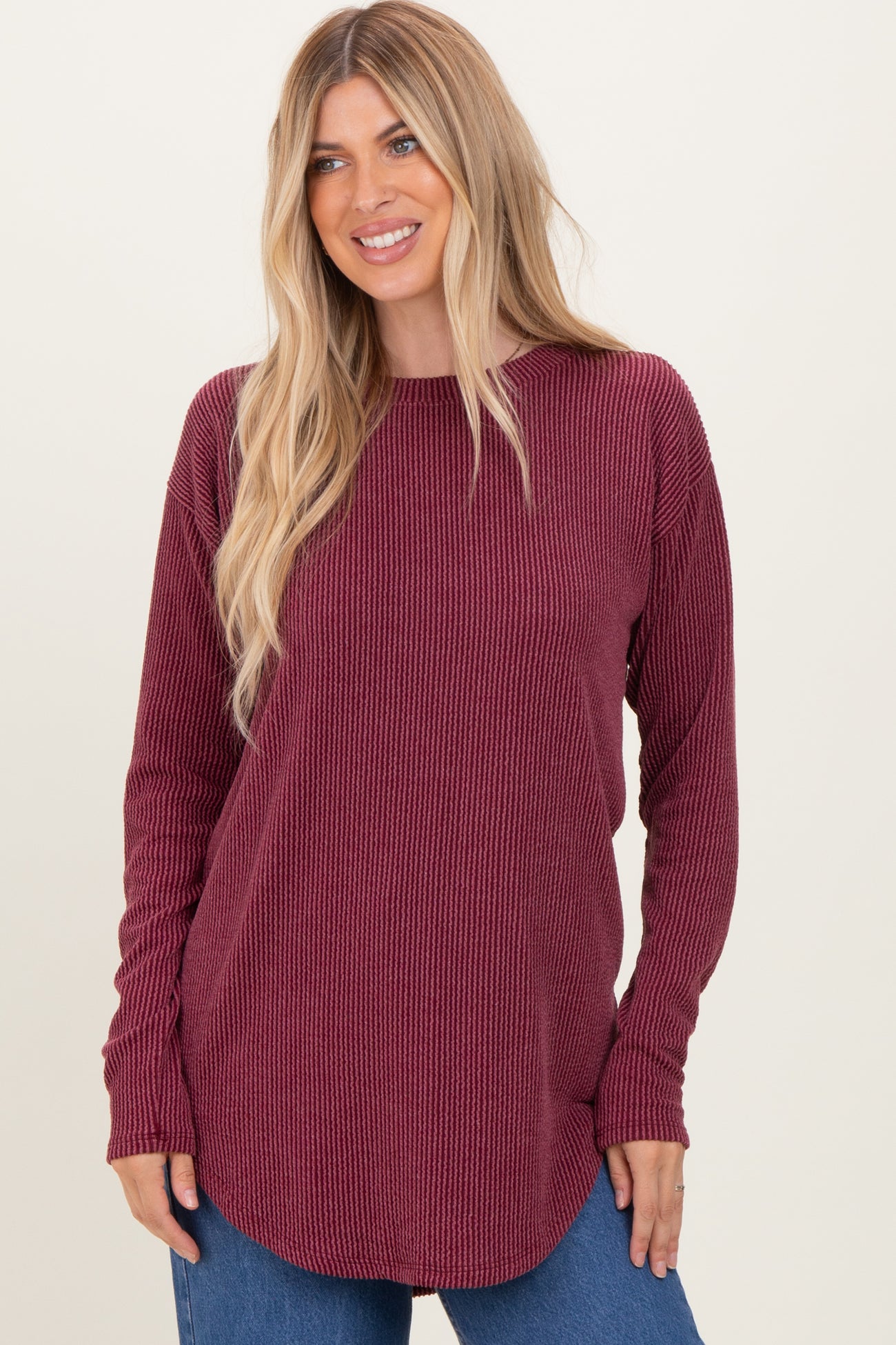 woman wearing a burgundy long sleeve ribbed top with a rounded hem and relaxed fit