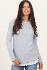 woman wearing a light gray long sleeve top with scalloped hem details and layered look, paired with blue jeans