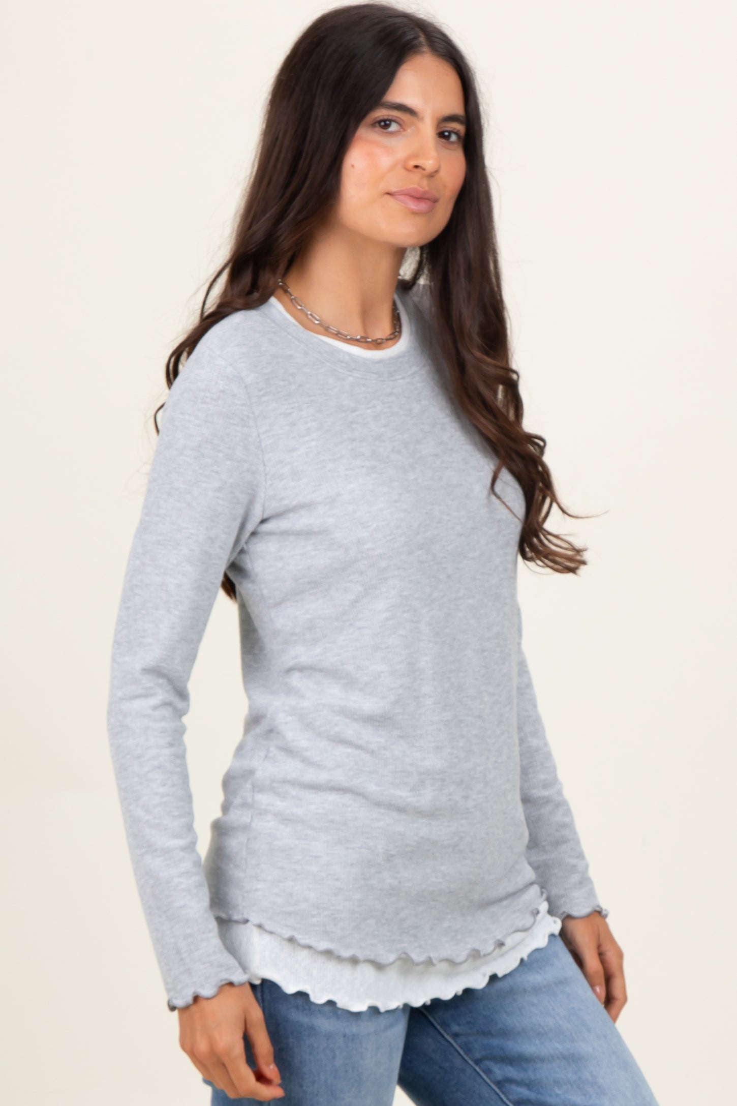 woman wearing a light gray long sleeve top with scalloped hem and casual jeans