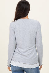 woman wearing a gray long sleeve top with a scalloped hem and a layered look, seen from the back