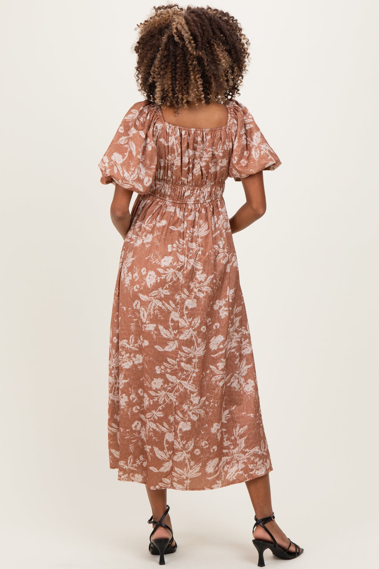 woman wearing a rust floral maternity dress with puff sleeves and smocked back, showing the back view