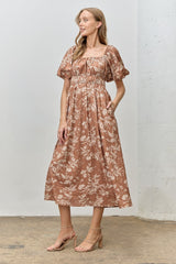 woman wearing a rust floral print midi dress with puff sleeves and a smocked bodice, standing against a neutral background