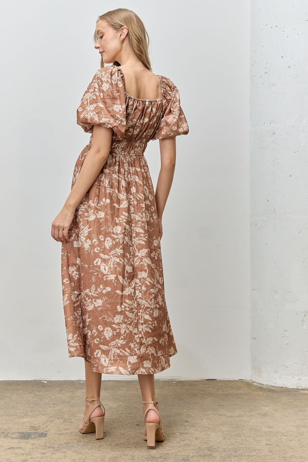 woman wearing a brown floral puff sleeve midi dress, featuring a smocked back and a relaxed fit