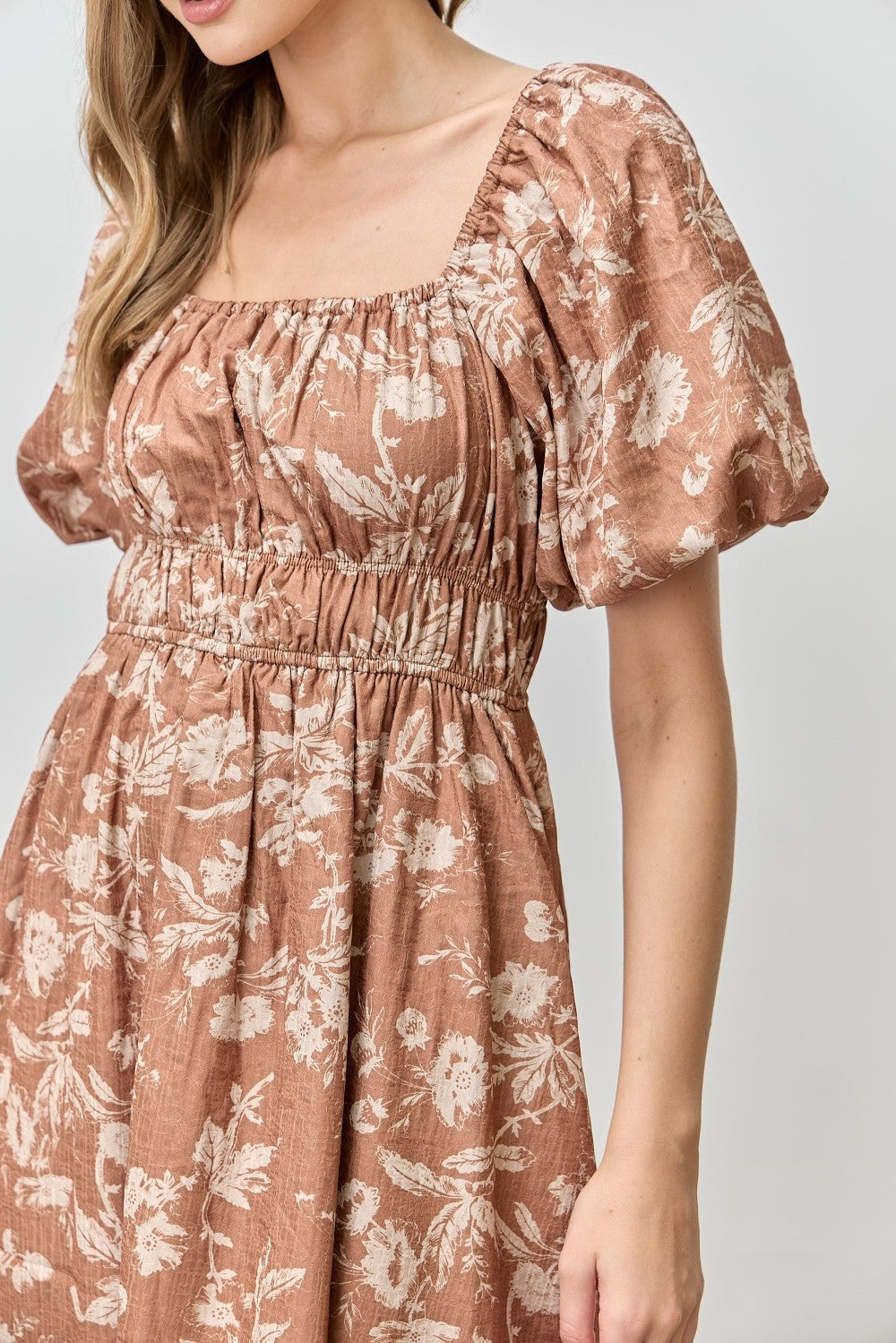 woman wearing a rust floral puff sleeve dress with a square neckline and smocked waist