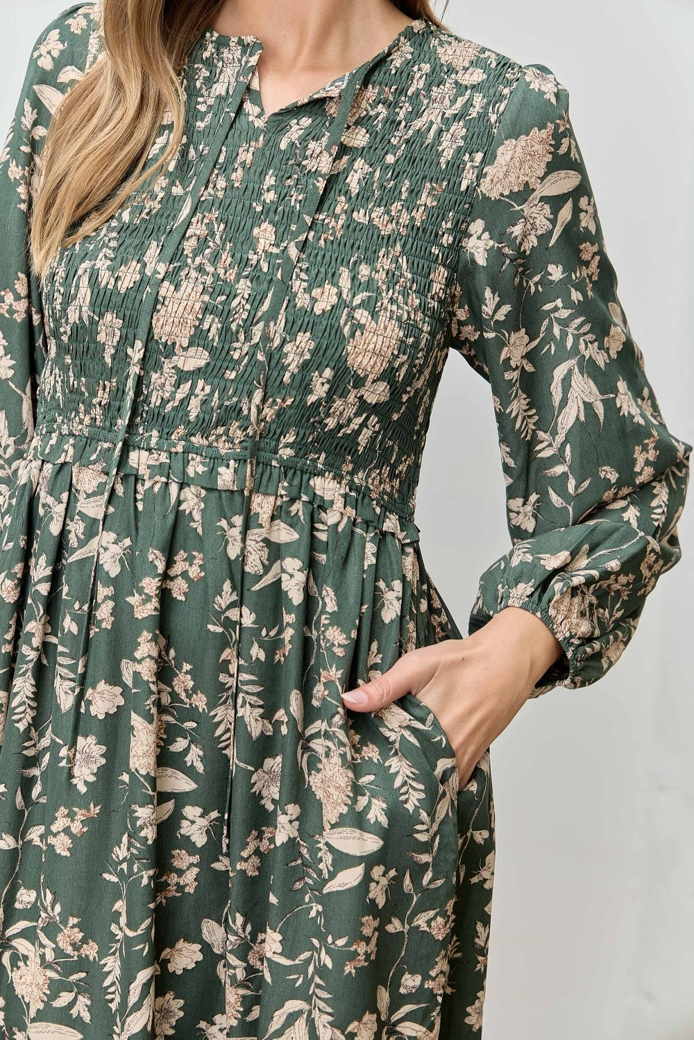 woman wearing a green floral long sleeve dress with smocked bodice and pockets