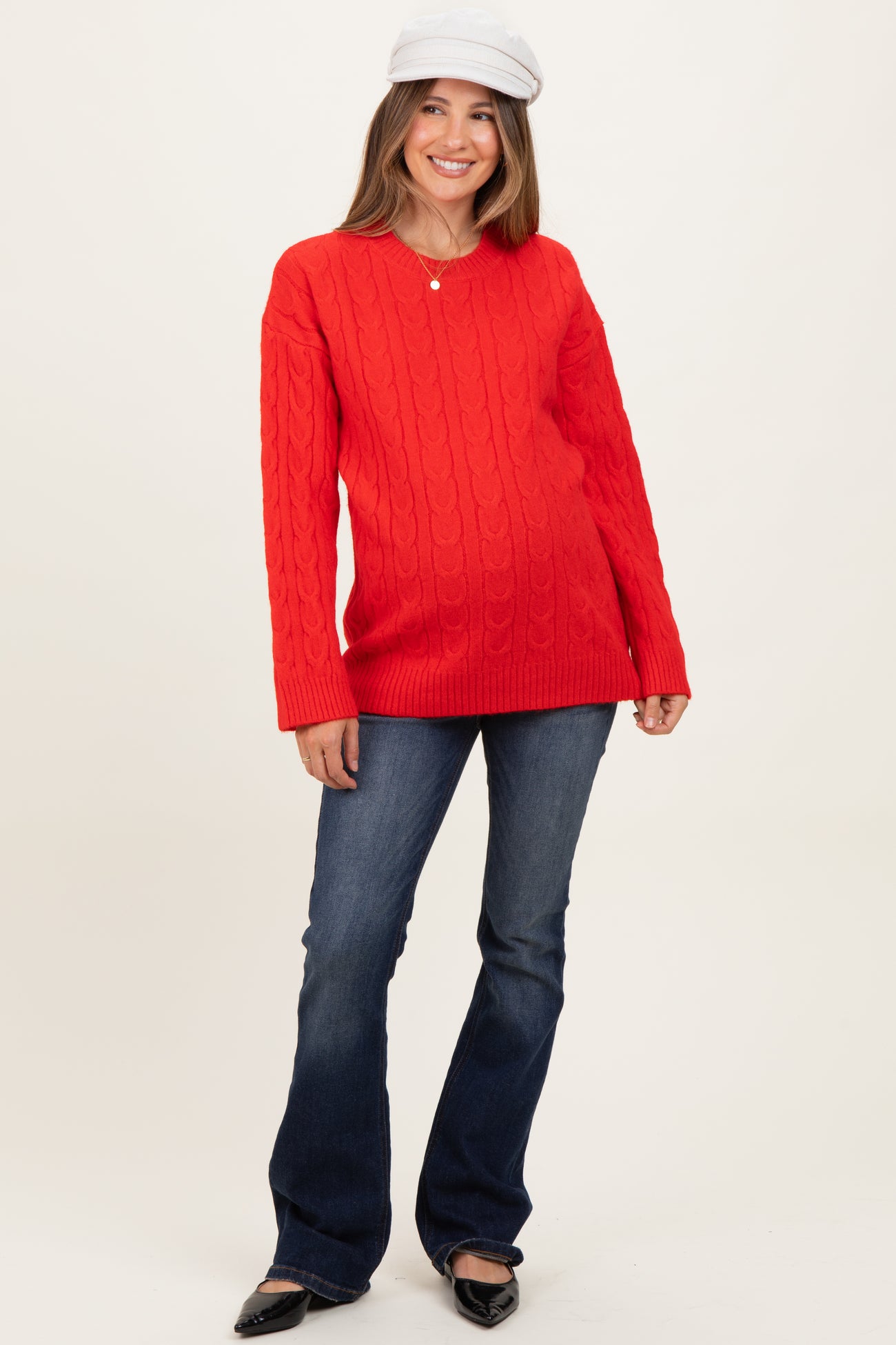woman wearing a red cable knit maternity sweater with a v-neck and blue flared jeans, showcasing a baby bump