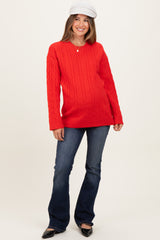 woman wearing a red cable knit maternity sweater with a v-neck and blue flared jeans, showcasing a baby bump