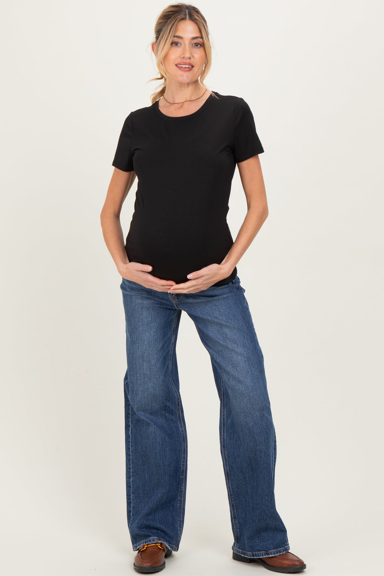 woman wearing a black short sleeve maternity top and blue flared jeans, cradling her baby bump