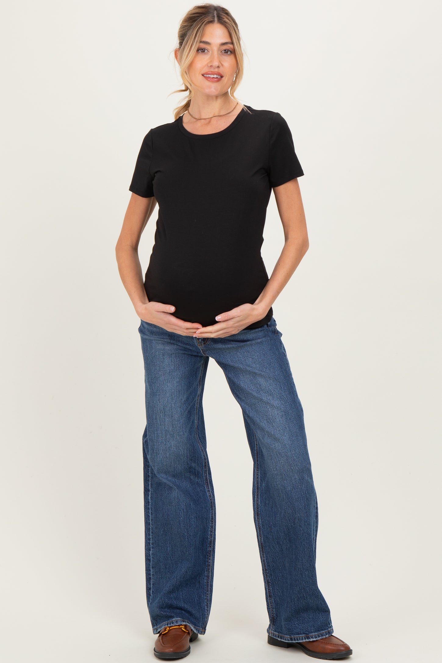 woman wearing a black short sleeve maternity top and blue flared jeans, cradling her baby bump