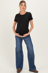 woman wearing a black short sleeve maternity top and blue flared jeans, cradling her baby bump