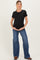 woman wearing a black short sleeve maternity top and blue flared jeans, cradling her baby bump