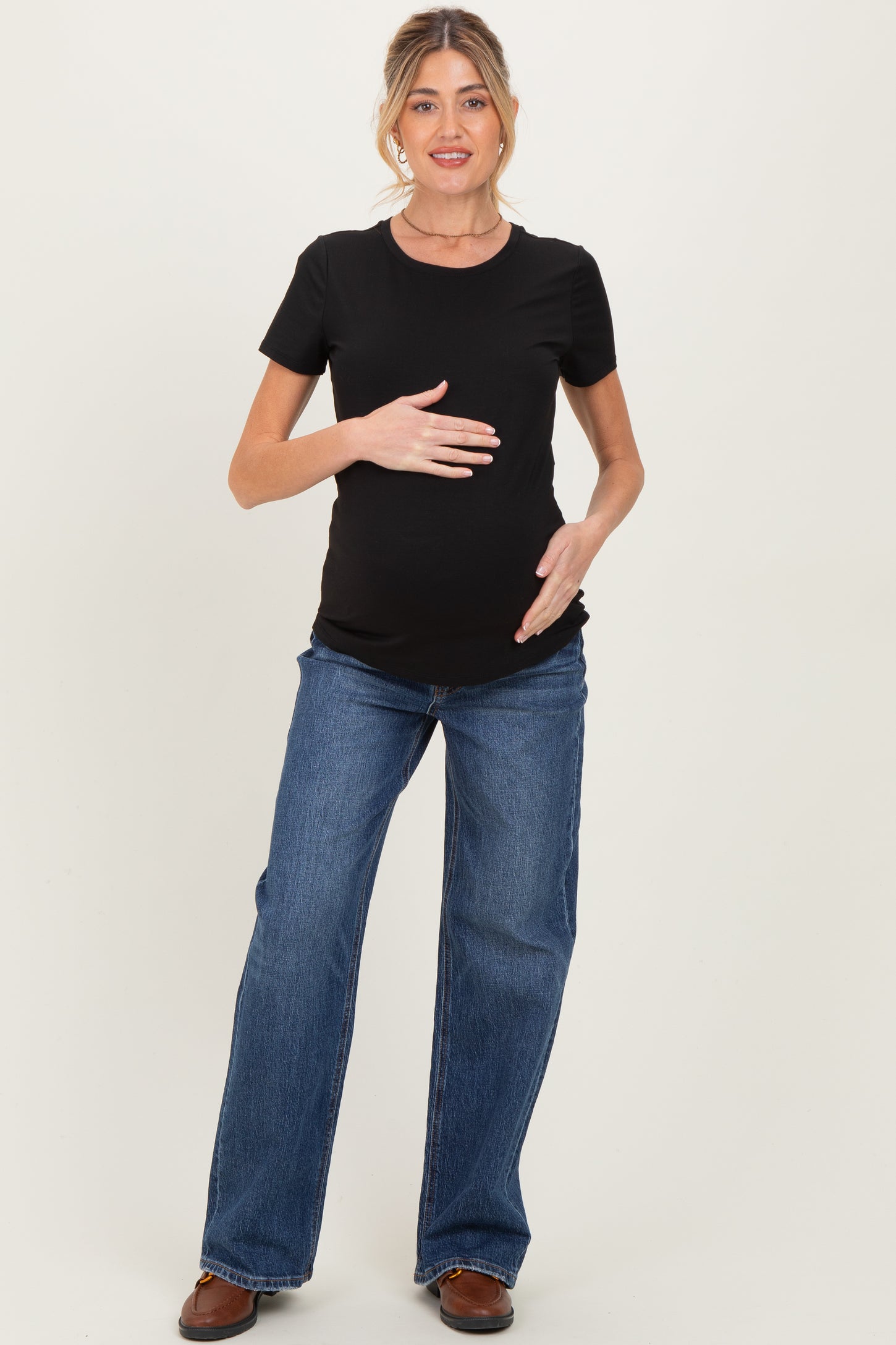 woman wearing a black short sleeve maternity top and blue flared jeans, holding her baby bump