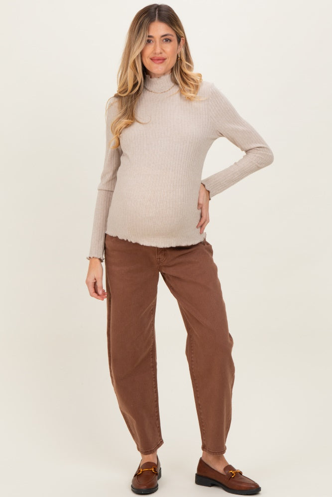 woman wearing a beige ribbed maternity turtleneck sweater and brown maternity jeans, showing her baby bump