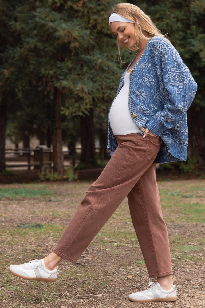 woman wearing a blue patterned maternity cardigan and brown maternity jeans, showing her baby bump, paired with white sneakers