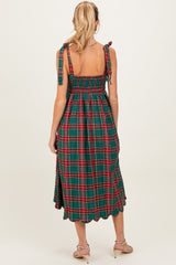 woman wearing a green and red plaid maternity dress with tie straps and a smocked back