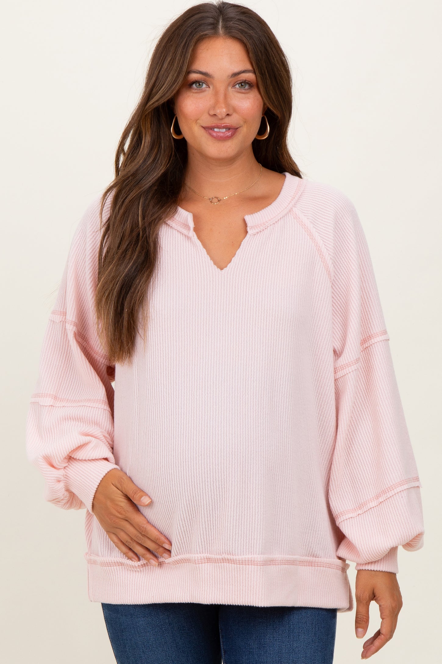 woman wearing a light pink maternity sweater with a v-neck and balloon sleeves, holding her baby bump