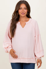 woman wearing a light pink maternity sweater with a v-neck and balloon sleeves, holding her baby bump