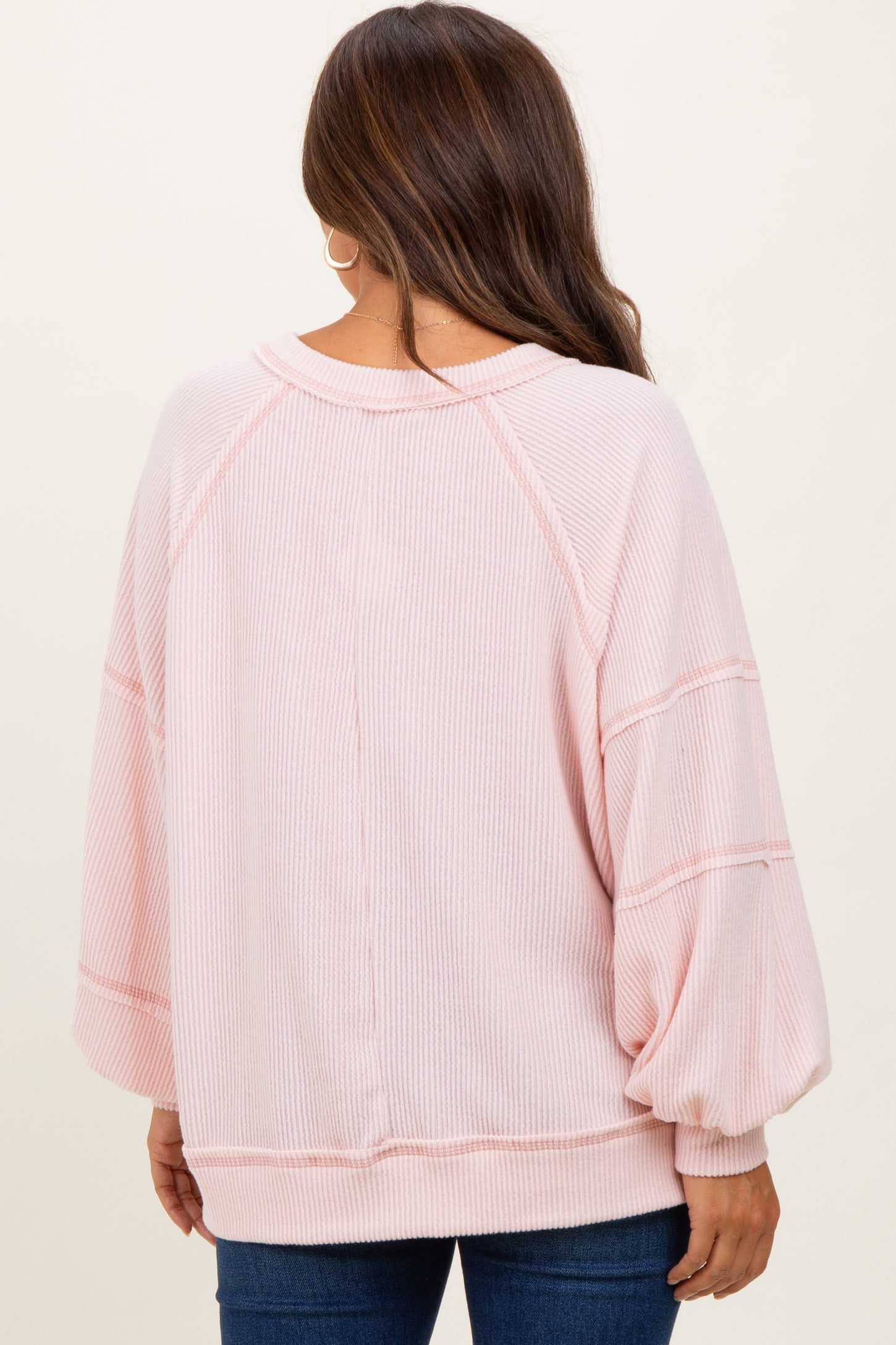 woman wearing a light pink oversized maternity sweater with balloon sleeves and ribbed texture, view from the back