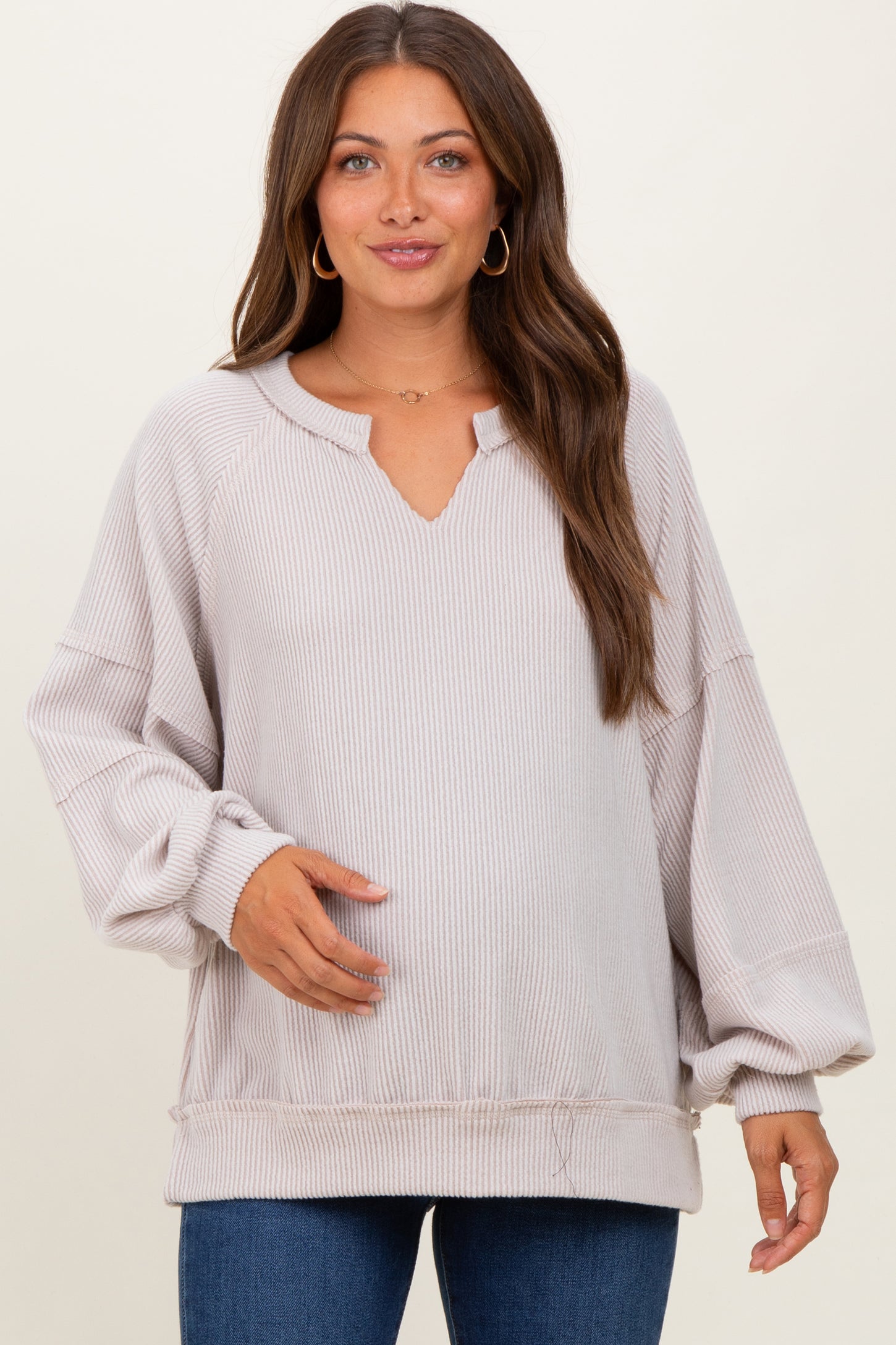 woman wearing a light taupe maternity pullover sweater with a v-neck and balloon sleeves, showing her baby bump