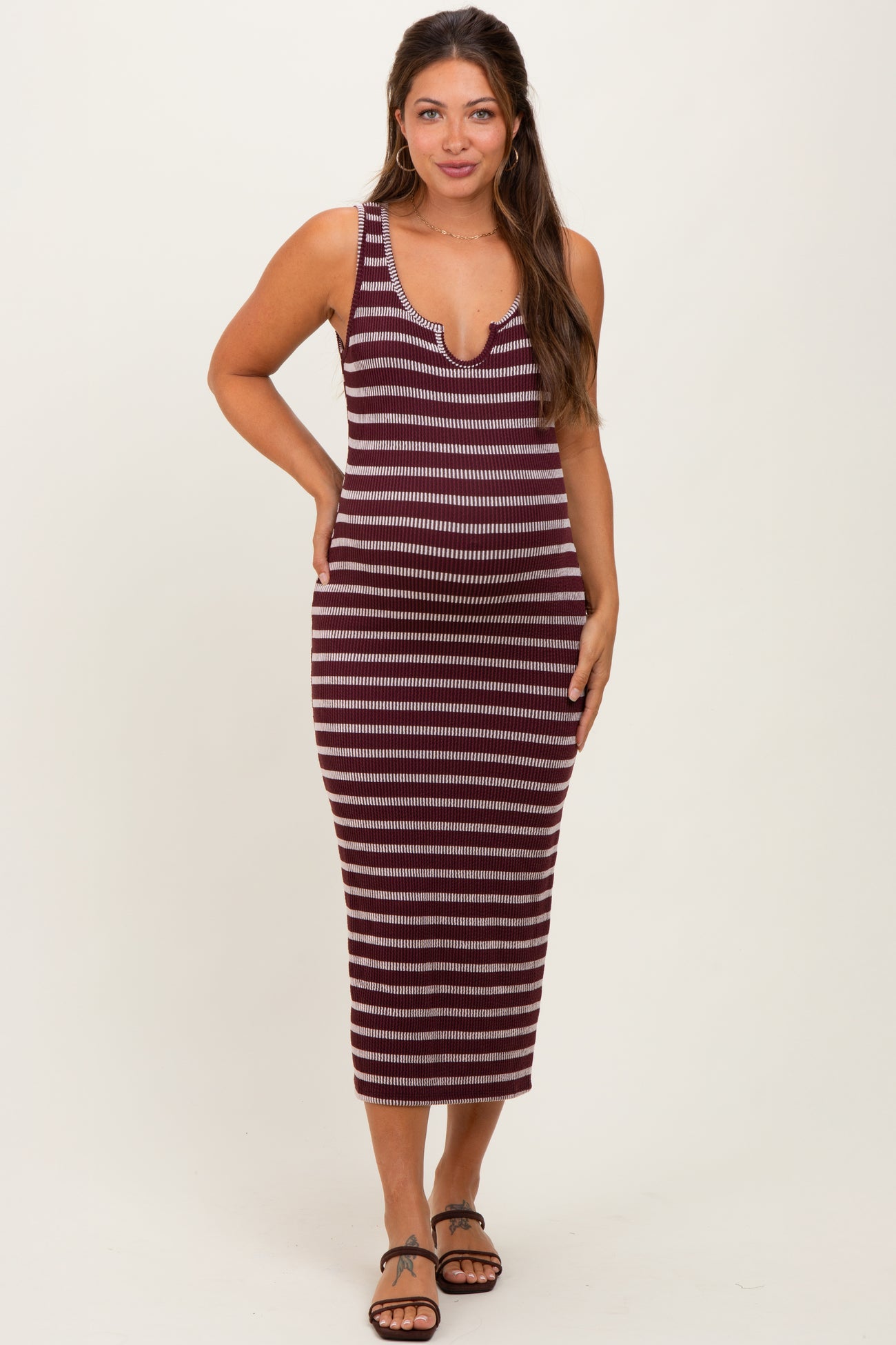 woman wearing a burgundy and cream striped maternity tank dress with a deeper v-neckline and a fitted silhouette
