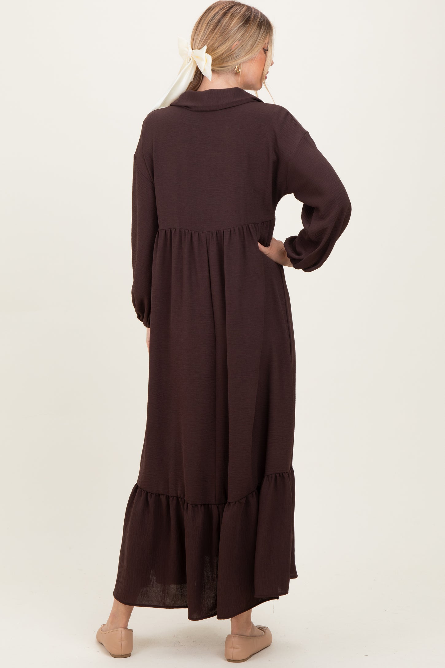 woman wearing a long brown tiered maxi dress with a collared neck and long sleeves, viewed from the back