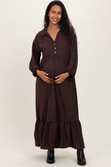woman wearing a brown maternity dress with a button-up collar and tiered skirt, gently cradling her baby bump