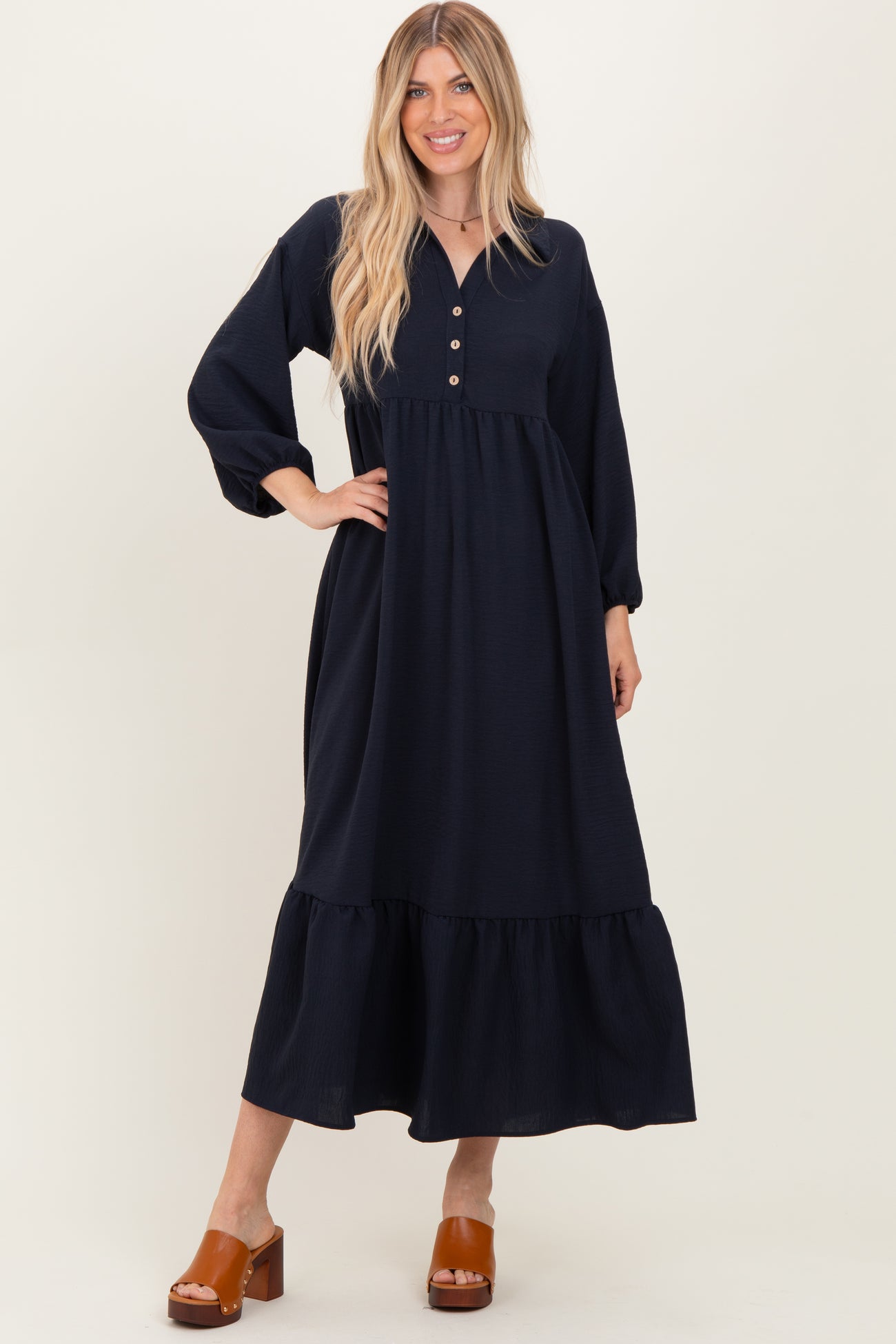 woman wearing a navy blue button-down maxi dress with long sleeves and a tiered skirt, paired with brown chunky heeled sandals