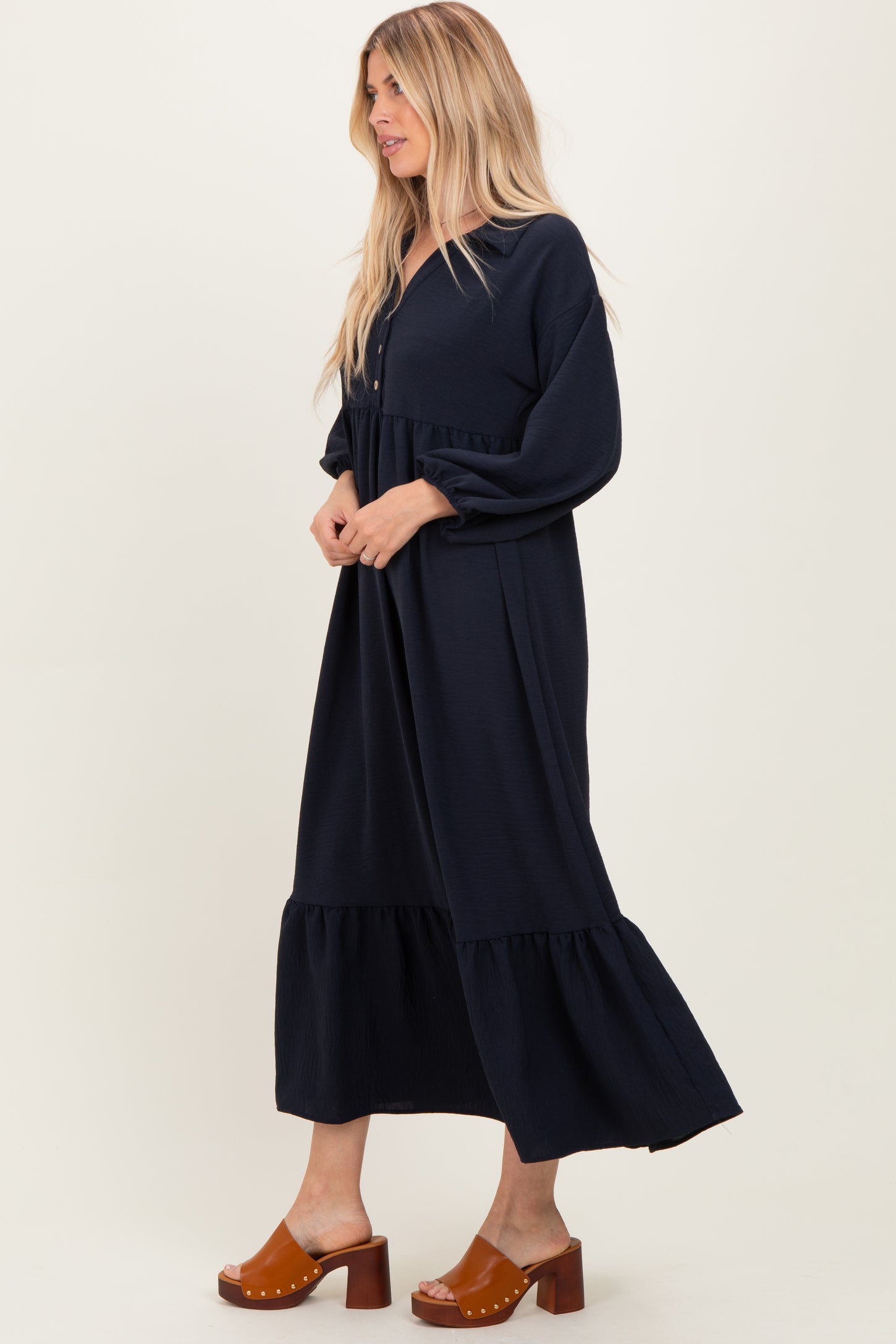 woman wearing a navy blue long sleeve maxi dress with a tiered hem and button details, standing sideways