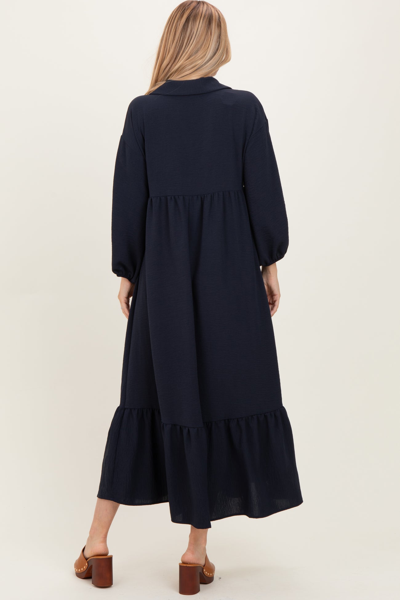 woman wearing a navy blue long sleeve maxi dress with a tiered ruffle hem and a collared neckline