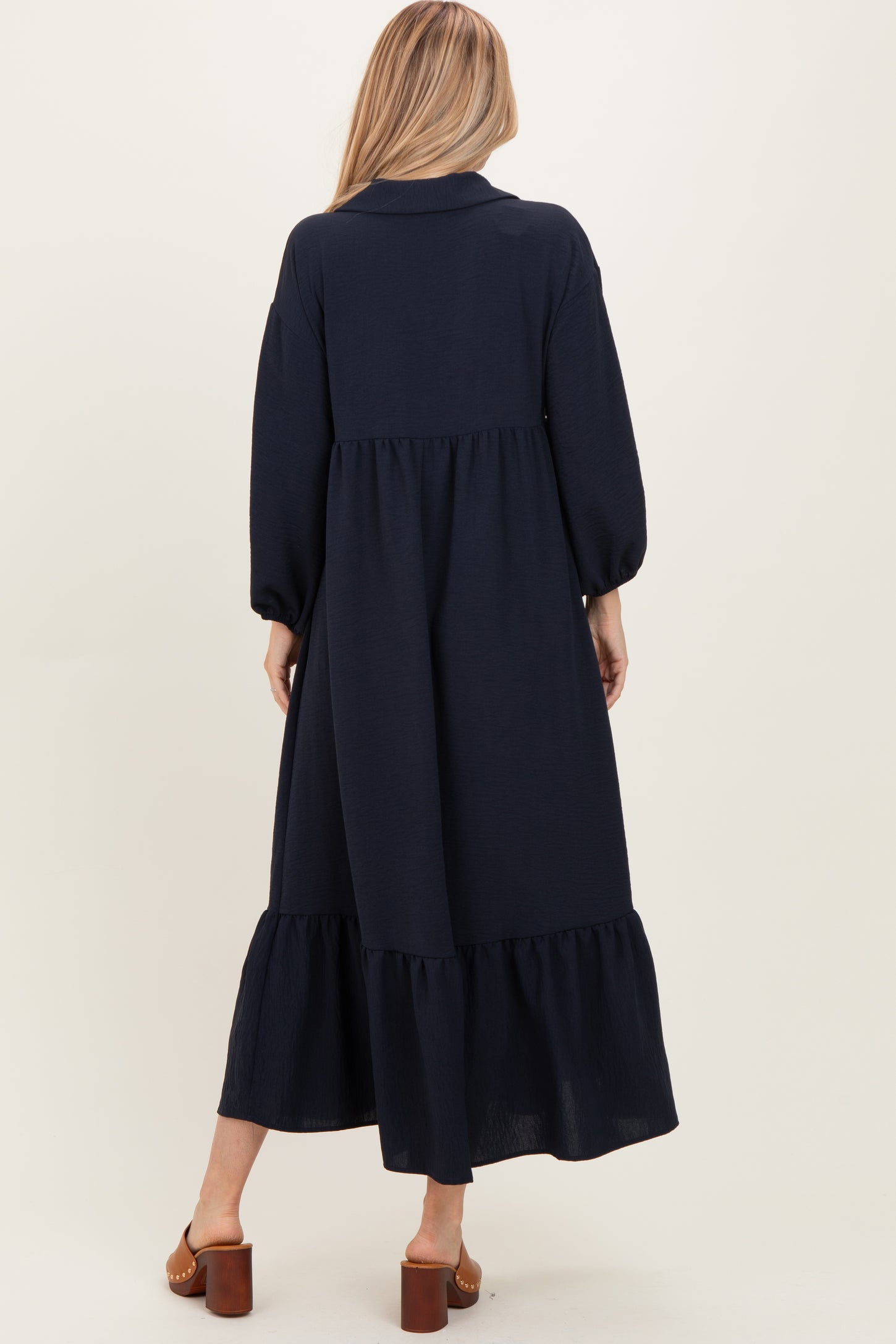 woman wearing a navy blue long sleeve maxi dress with a tiered ruffle hem and a collared neckline
