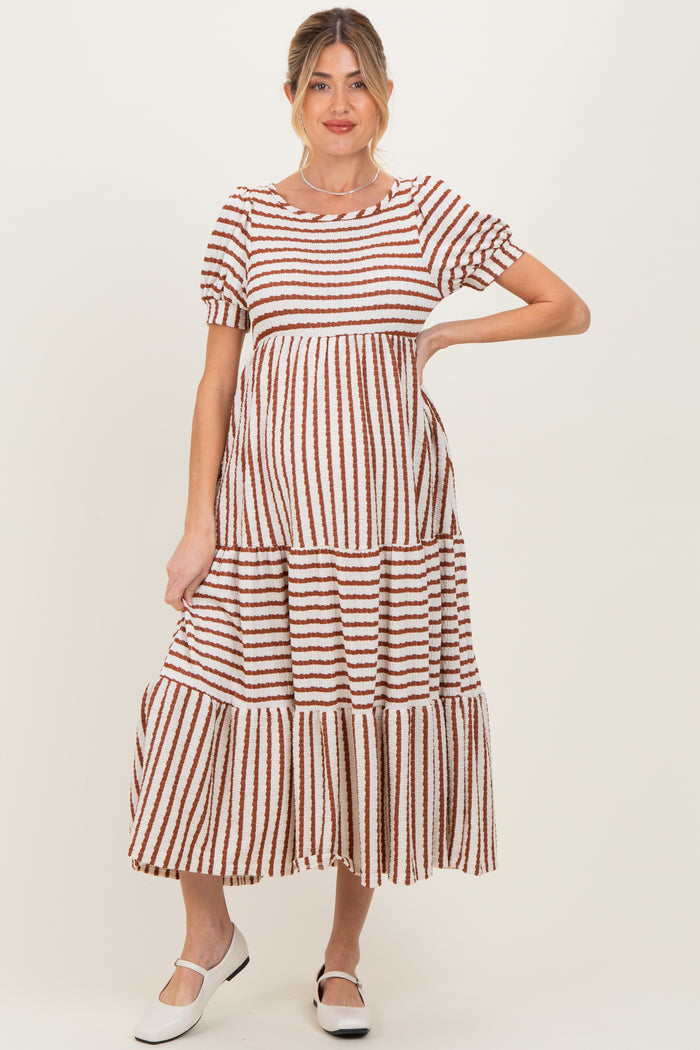 woman wearing a brown and white striped maternity maxi dress with short sleeves and a tiered skirt, showing her baby bump
