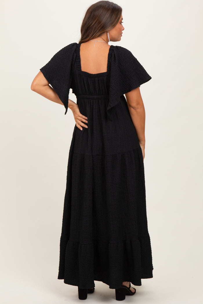 woman wearing a black maternity maxi dress with short flutter sleeves and tiered ruffle details, back view