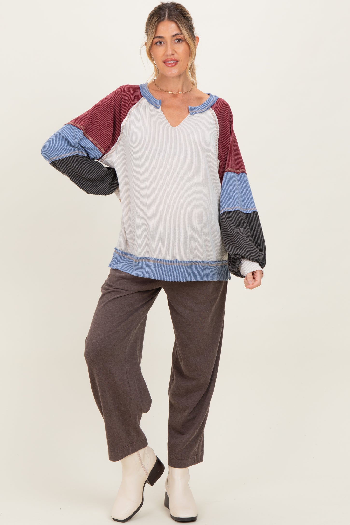 woman wearing a color-blocked maternity top with a v-neck and long sleeves, paired with gray wide-leg pants and a baby bump visible