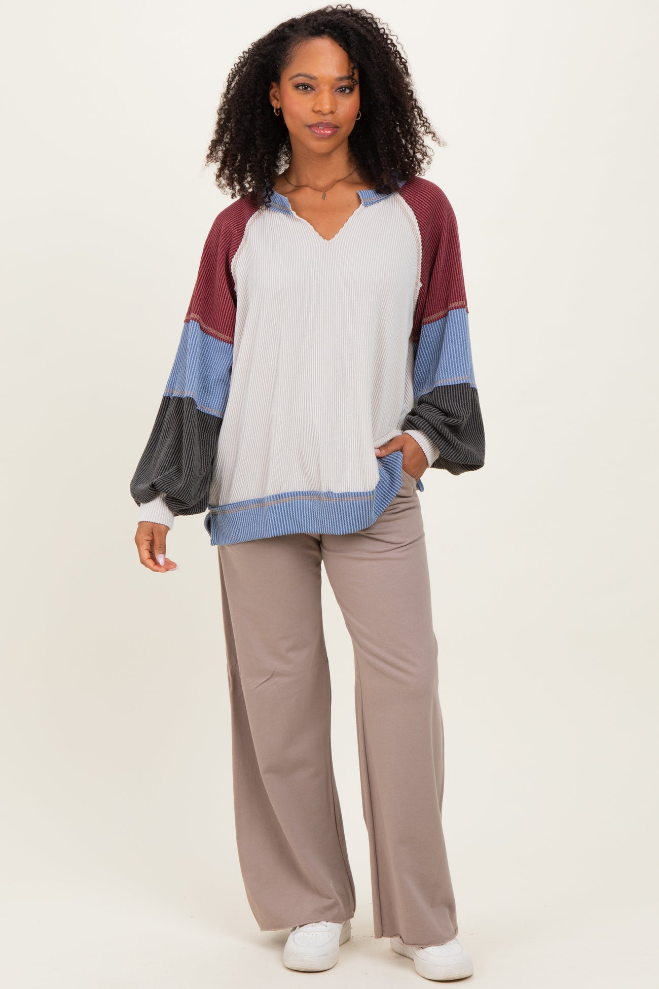 woman wearing a multi-colored long sleeve top with a v-neck and loose fit, paired with light brown wide-leg pants