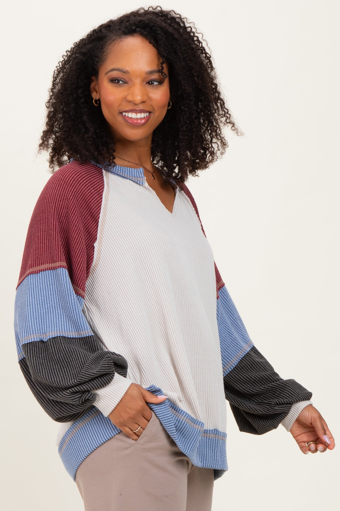 woman wearing a color block long sleeve oversized top in cream, red, blue, and black with a v-neck and loose fit
