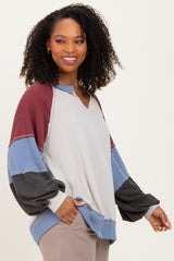 woman wearing a color block long sleeve oversized top in cream, red, blue, and black with a v-neck and loose fit