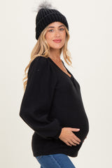 woman wearing a black maternity sweater with a v-neck and puff sleeves, holding her baby bump