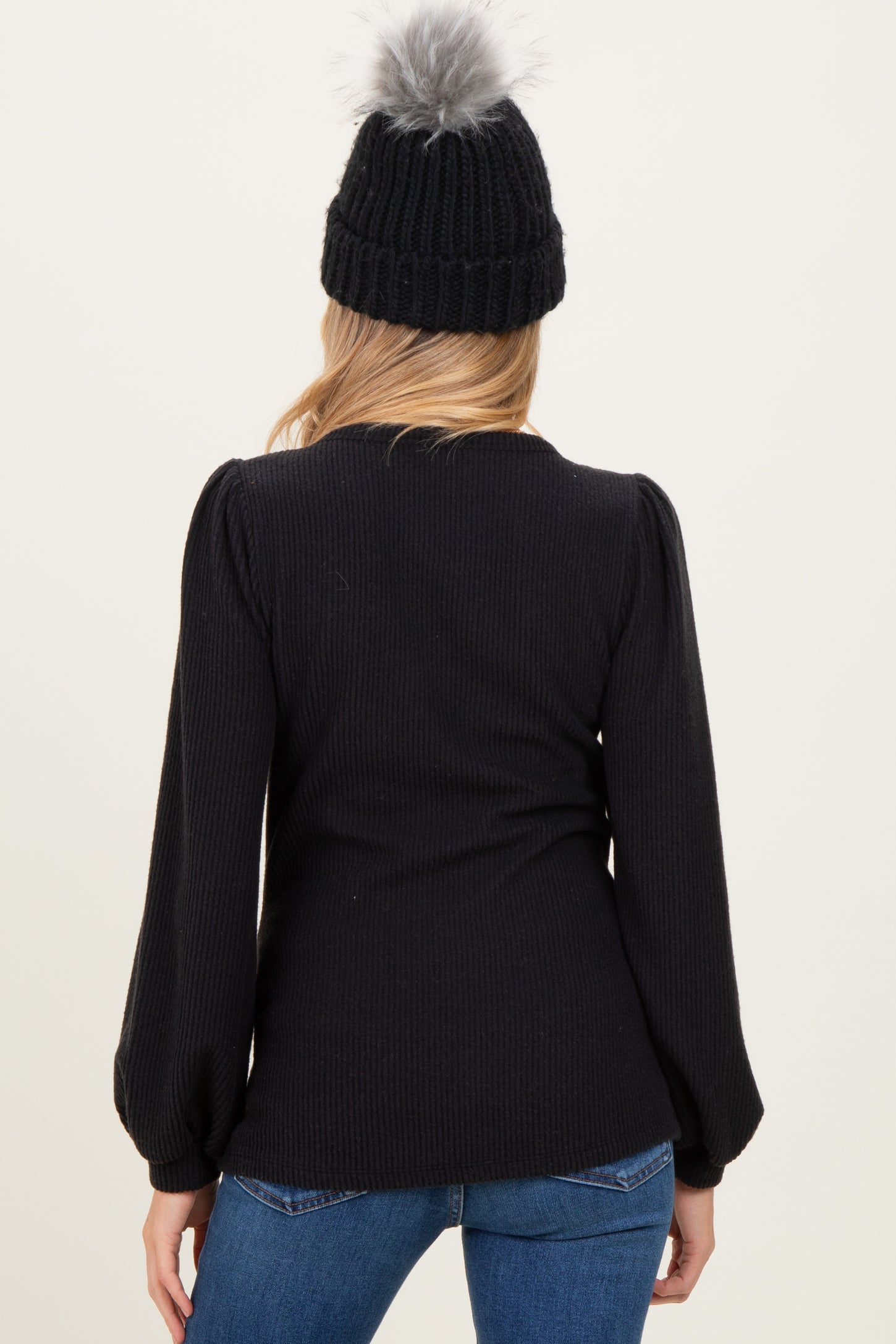 woman wearing a black ribbed maternity top with puffed sleeves, styled with blue jeans and a knit beanie