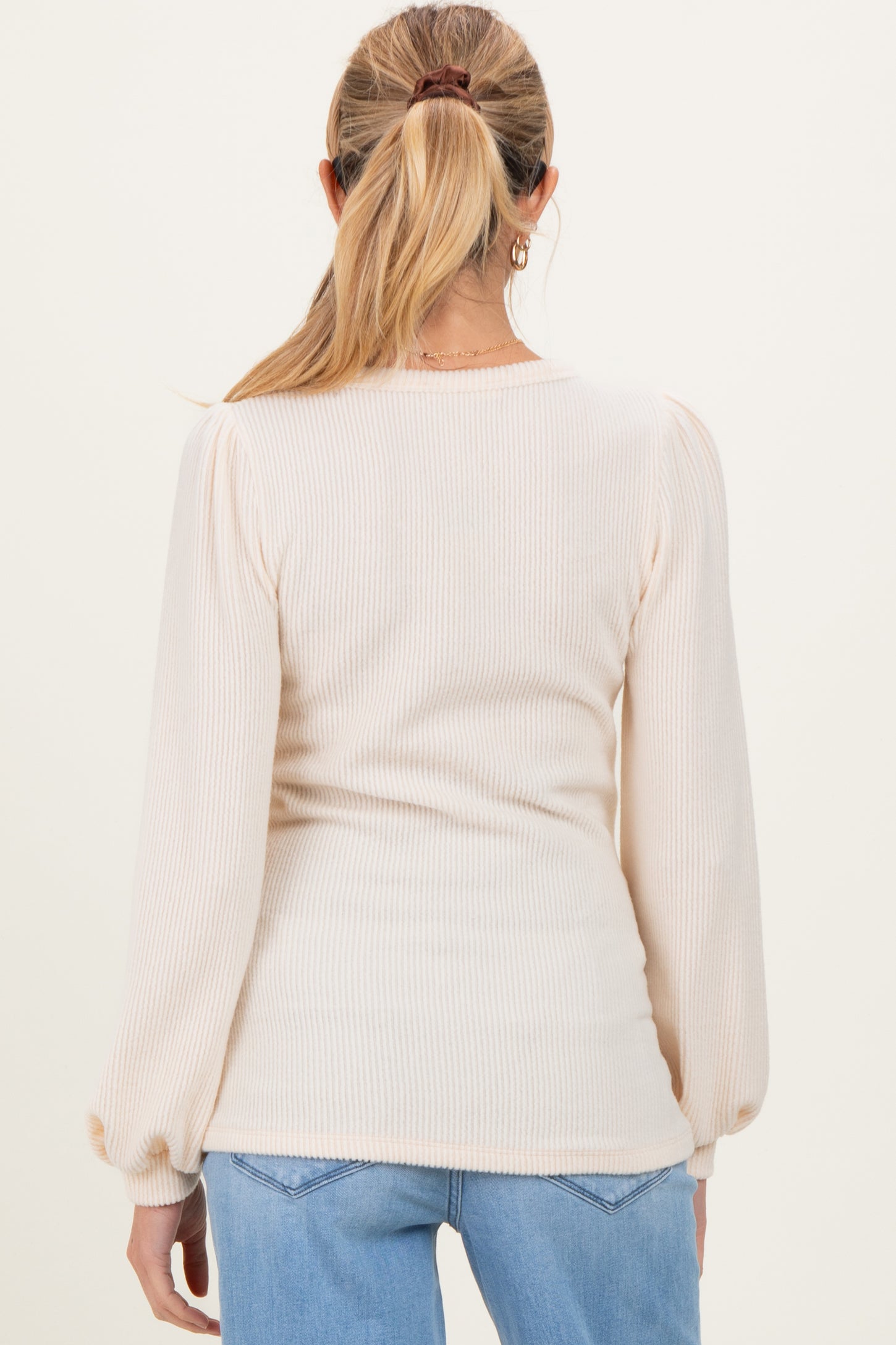 woman wearing a light beige ribbed maternity top with long puff sleeves, viewed from the back