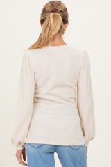 woman wearing a light beige ribbed maternity top with long puff sleeves, viewed from the back