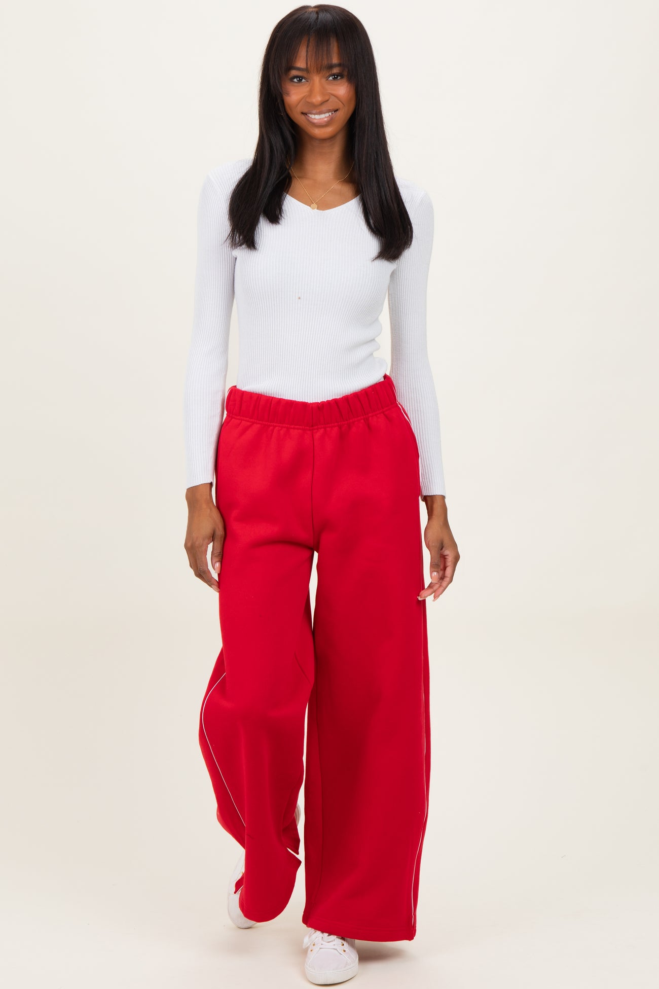 woman wearing a white long sleeve fitted top and red wide leg sweatpants with a casual pose